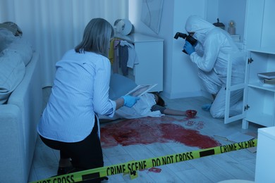 Forensic experts working at crime scene with dead woman's body indoors