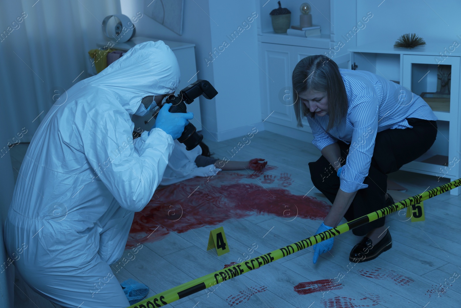 Photo of Forensic experts working at crime scene with dead woman's body indoors