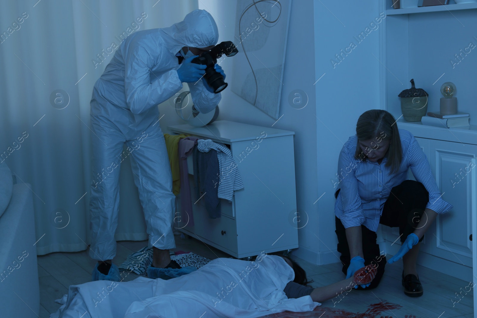 Photo of Forensic experts working at crime scene with dead woman's body indoors