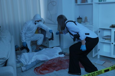 Photo of Forensic experts working at crime scene with dead woman's body indoors