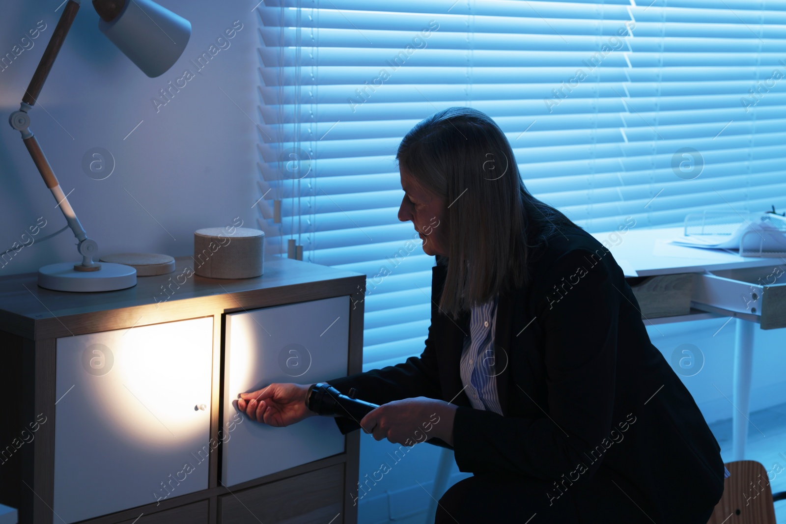 Photo of Forensic expert with flashlight working at crime scene indoors