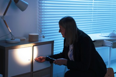 Forensic expert with flashlight working at crime scene indoors