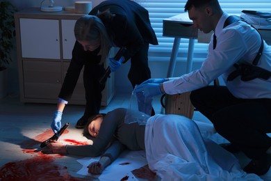 Photo of Forensic experts working at crime scene with dead woman's body indoors