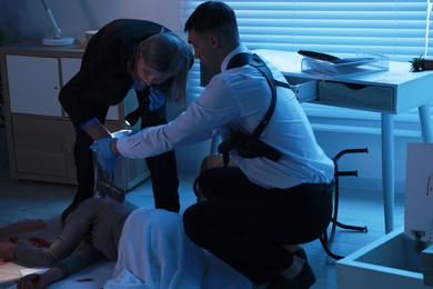 Photo of Forensic experts working at crime scene with dead woman's body indoors