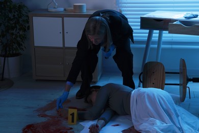 Photo of Forensic expert working at crime scene with dead woman's body indoors