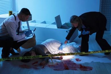 Photo of Forensic experts working at crime scene with dead woman's body indoors