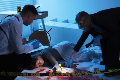 Forensic experts working at crime scene with dead woman's body indoors