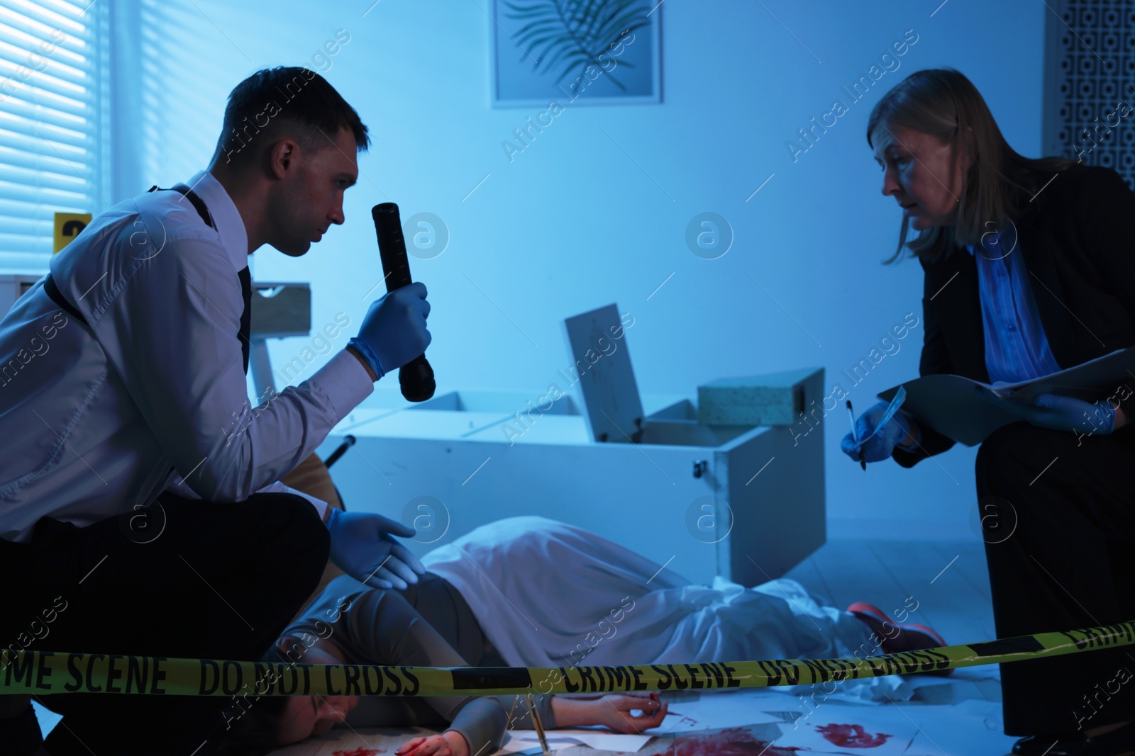 Photo of Forensic experts working at crime scene with dead woman's body indoors