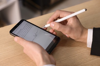 Photo of Electronic signature. Man using stylus and smartphone at wooden table, closeup