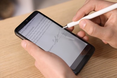 Photo of Electronic signature. Man using stylus and smartphone at wooden table, closeup