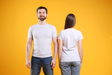 Woman and man wearing blank white t-shirts on orange background. Mockup for design