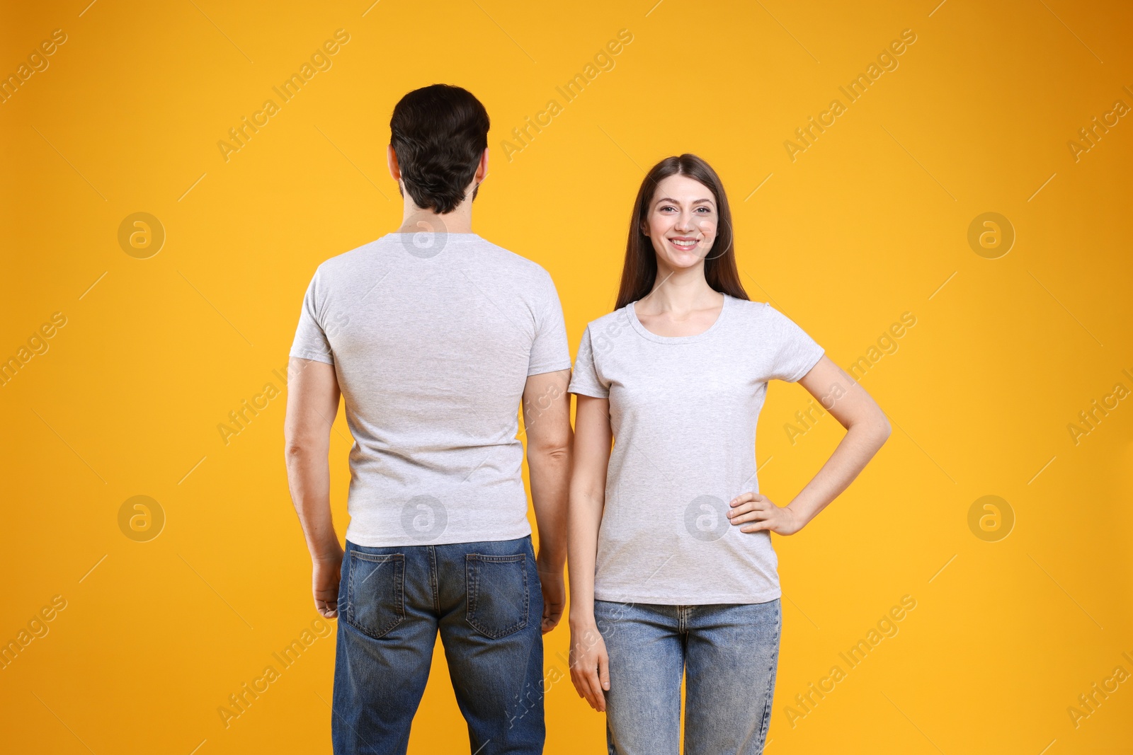 Photo of Woman and man wearing blank white t-shirts on orange background, back view. Mockup for design