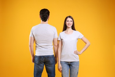 Woman and man wearing blank white t-shirts on orange background, back view. Mockup for design