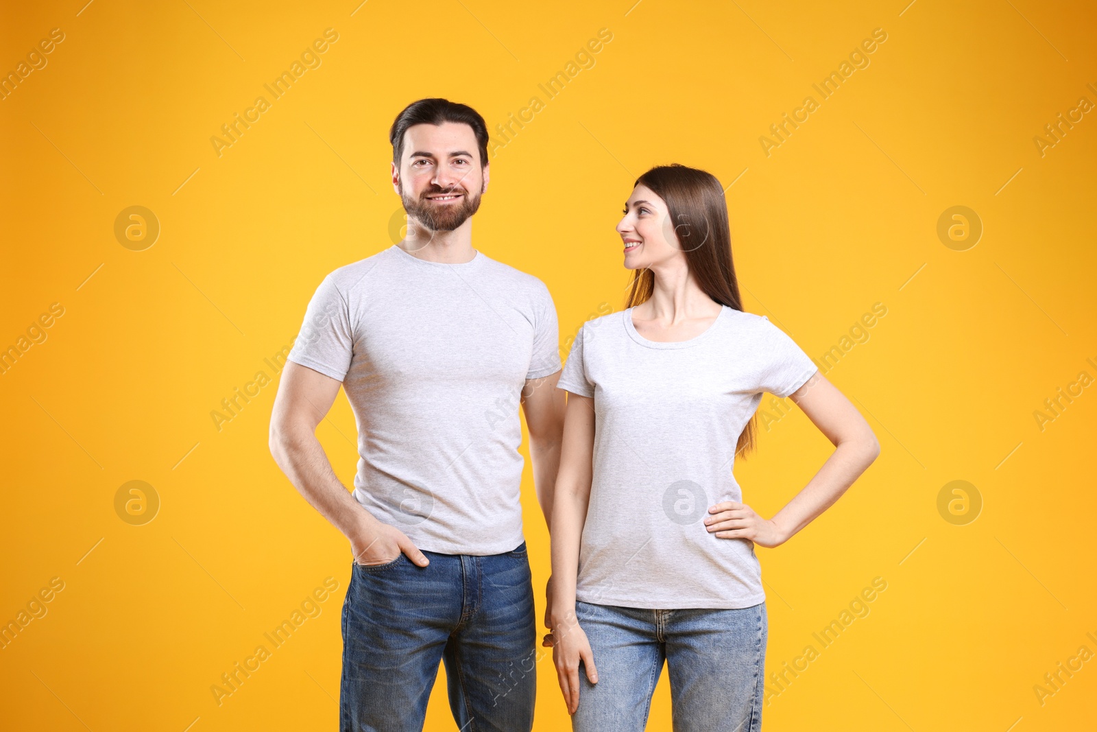 Photo of Woman and man wearing blank white t-shirts on orange background. Mockup for design