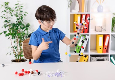 Photo of Boy showing DNA structure model at desk indoors