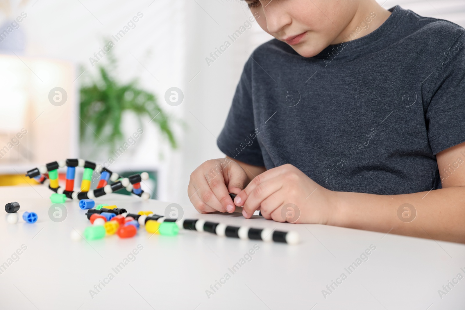 Photo of Boy making DNA structure model at desk indoors, closeup