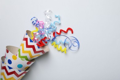 Photo of Colorful party hats and streamers on light grey background, flat lay. Space for text