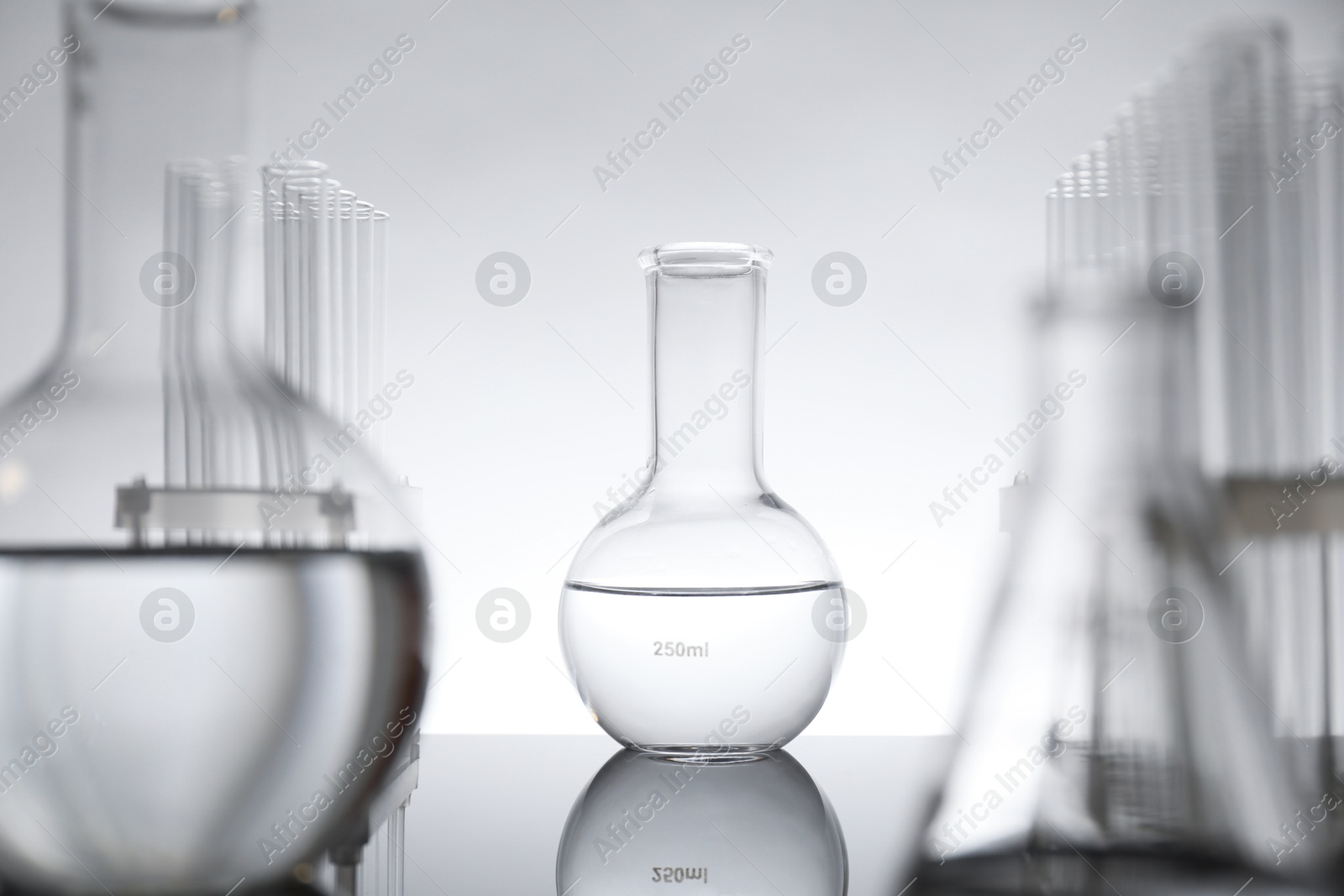 Photo of Laboratory glassware with liquid on mirror surface against light background