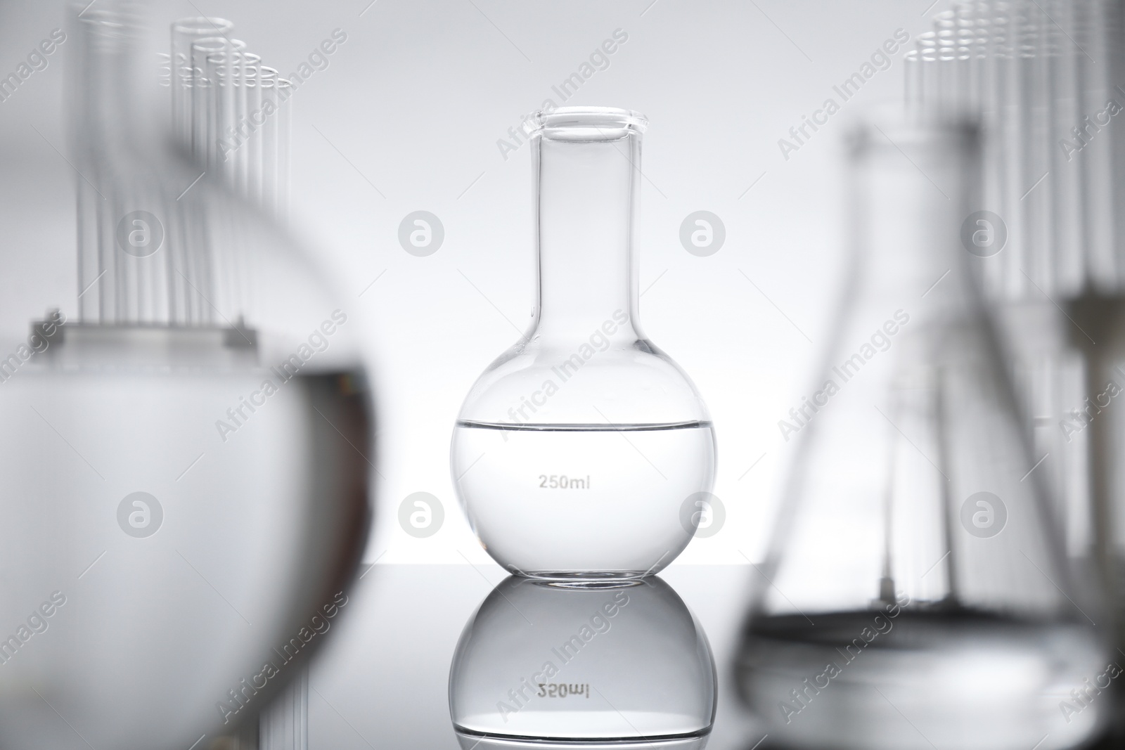 Photo of Laboratory glassware with liquid on mirror surface against light background