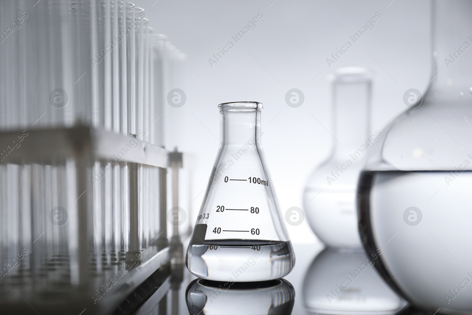 Photo of Laboratory glassware with liquid on mirror surface against light background