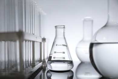 Laboratory glassware with liquid on mirror surface against light background