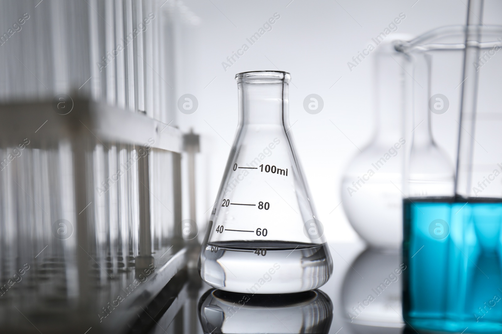 Photo of Laboratory glassware with liquid on mirror surface against light background