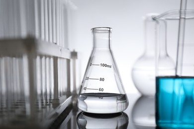 Photo of Laboratory glassware with liquid on mirror surface against light background