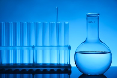 Photo of Laboratory glassware with liquid on mirror surface against light blue background