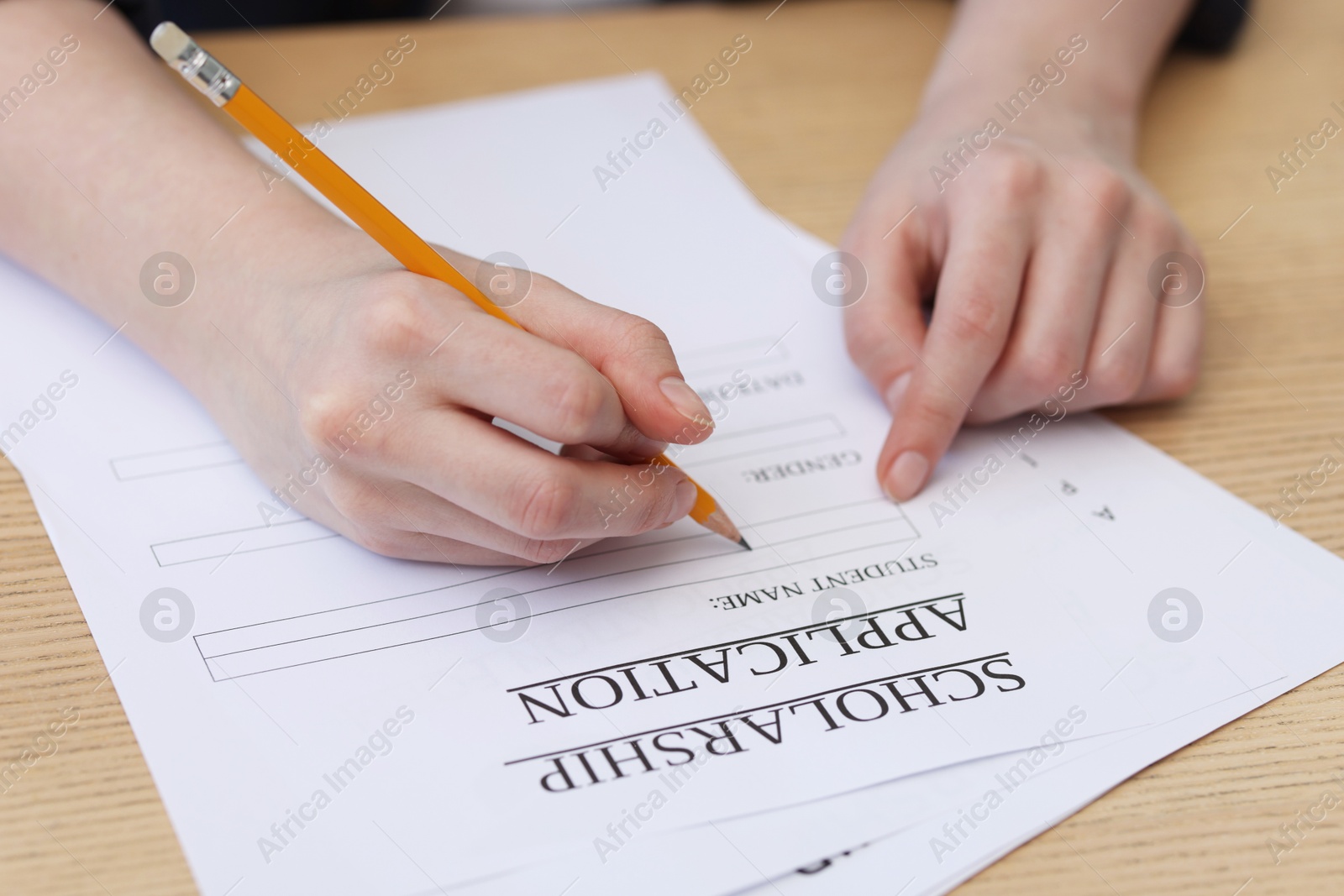 Photo of Student filling scholarship application form at wooden table, closeup