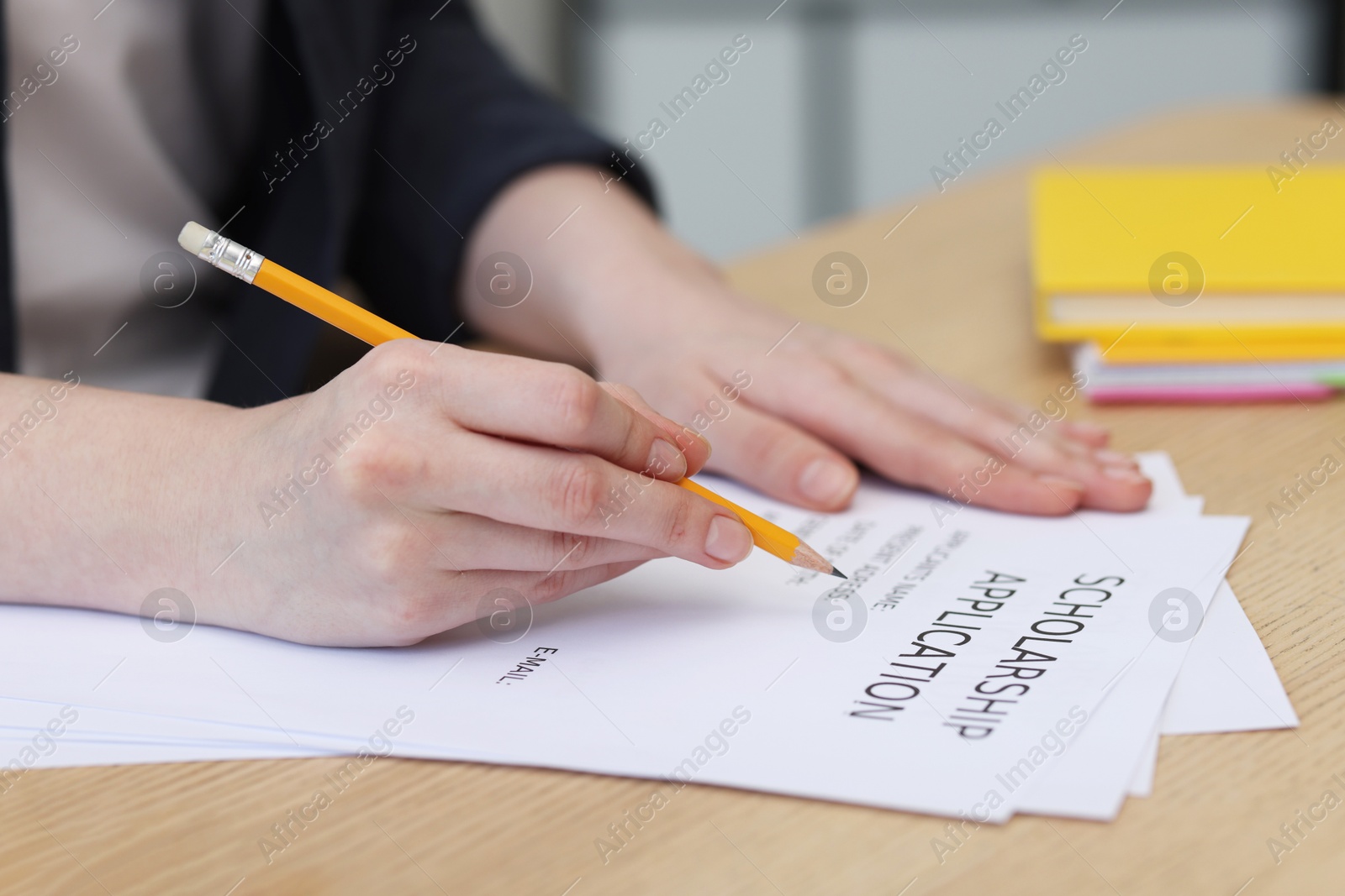 Photo of Student filling scholarship application form at wooden table, closeup