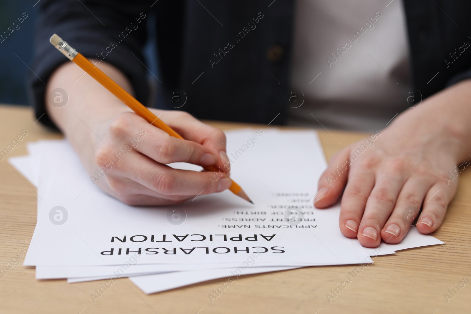 Photo of Student filling scholarship application form at wooden table, closeup