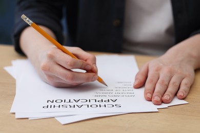 Student filling scholarship application form at wooden table, closeup