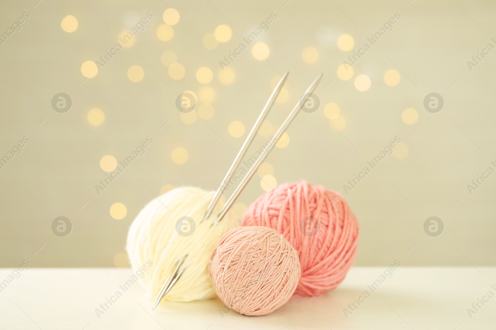 Photo of Balls of colorful yarn and knitting needles on white table against grey background with blurred lights, bokeh effect