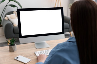 Photo of Woman looking at monitor with blank screen at wooden table indoors. Mockup for design