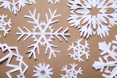 Photo of Beautiful paper snowflakes on brown background, flat lay