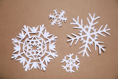 Photo of Beautiful paper snowflakes on brown background, flat lay