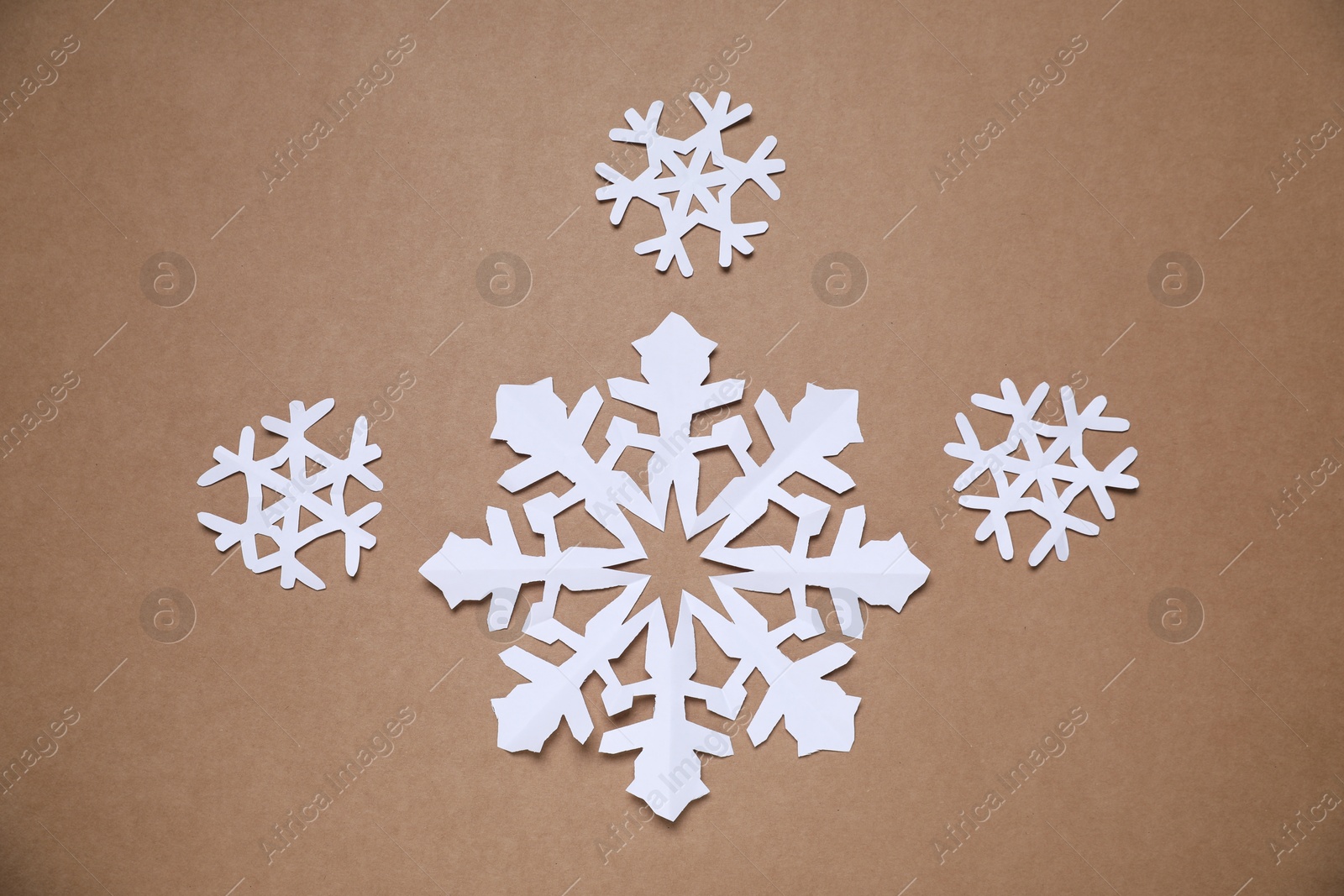 Photo of Beautiful paper snowflakes on brown background, flat lay