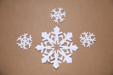 Photo of Beautiful paper snowflakes on brown background, flat lay