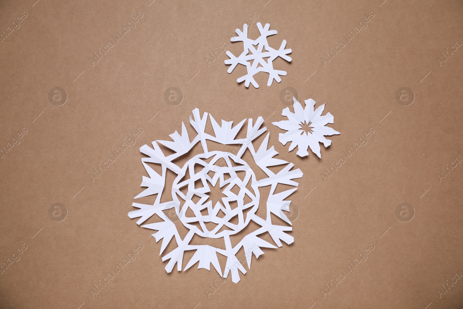 Photo of Beautiful paper snowflakes on brown background, flat lay