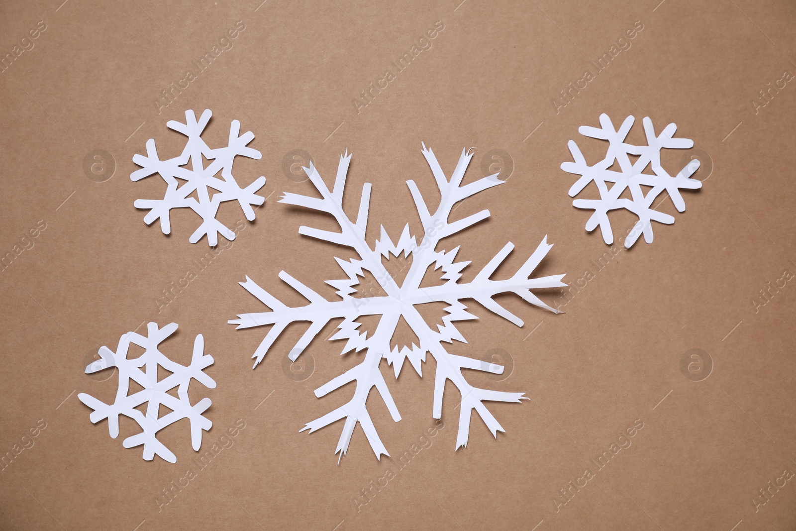 Photo of Beautiful paper snowflakes on brown background, flat lay