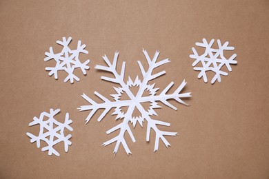 Photo of Beautiful paper snowflakes on brown background, flat lay