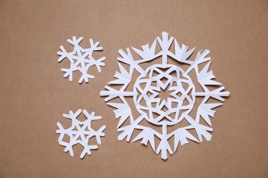 Photo of Beautiful paper snowflakes on brown background, flat lay