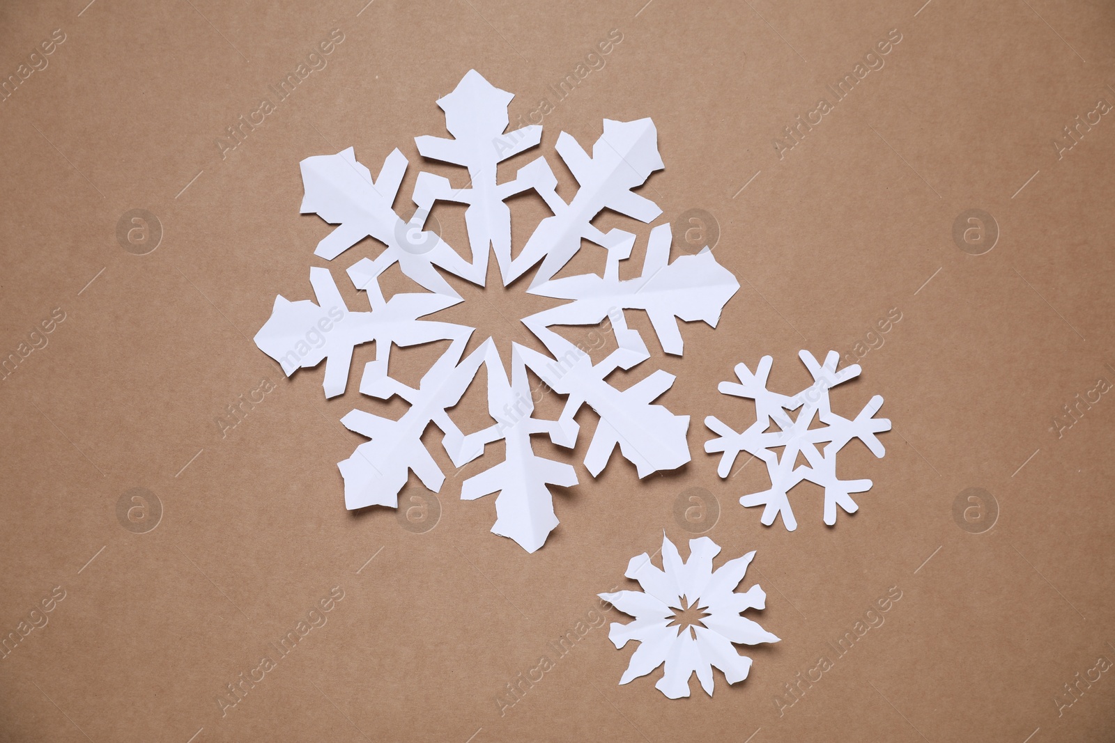 Photo of Beautiful paper snowflakes on brown background, flat lay