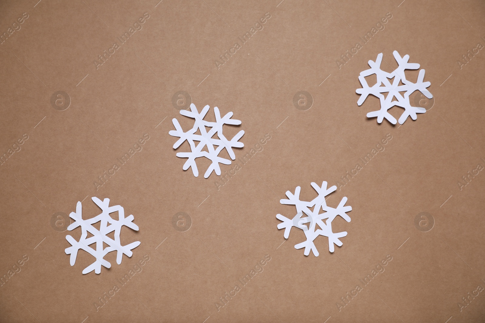 Photo of Beautiful paper snowflakes on brown background, flat lay