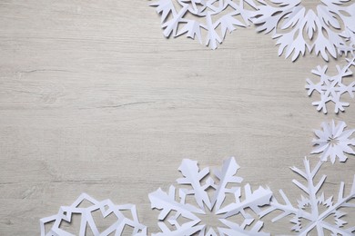 Photo of Beautiful paper snowflakes on white wooden background, flat lay. Space for text