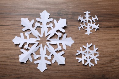 Photo of Beautiful paper snowflakes on wooden background, flat lay