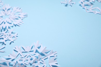 Photo of Beautiful paper snowflakes on light blue background, closeup. Space for text