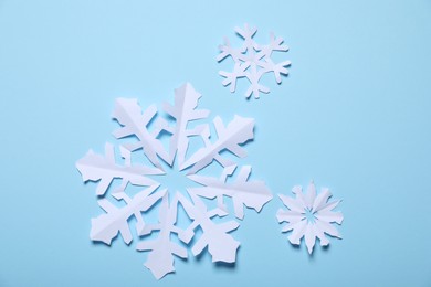 Photo of Beautiful paper snowflakes on light blue background, flat lay