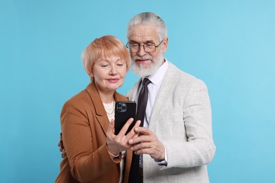 Lovely senior couple looking at smartphone on light blue background