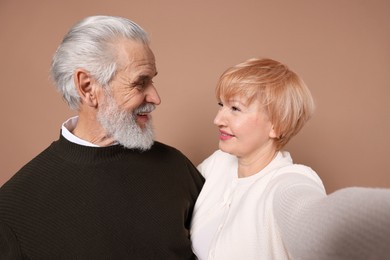 Lovely senior couple taking selfie on beige background